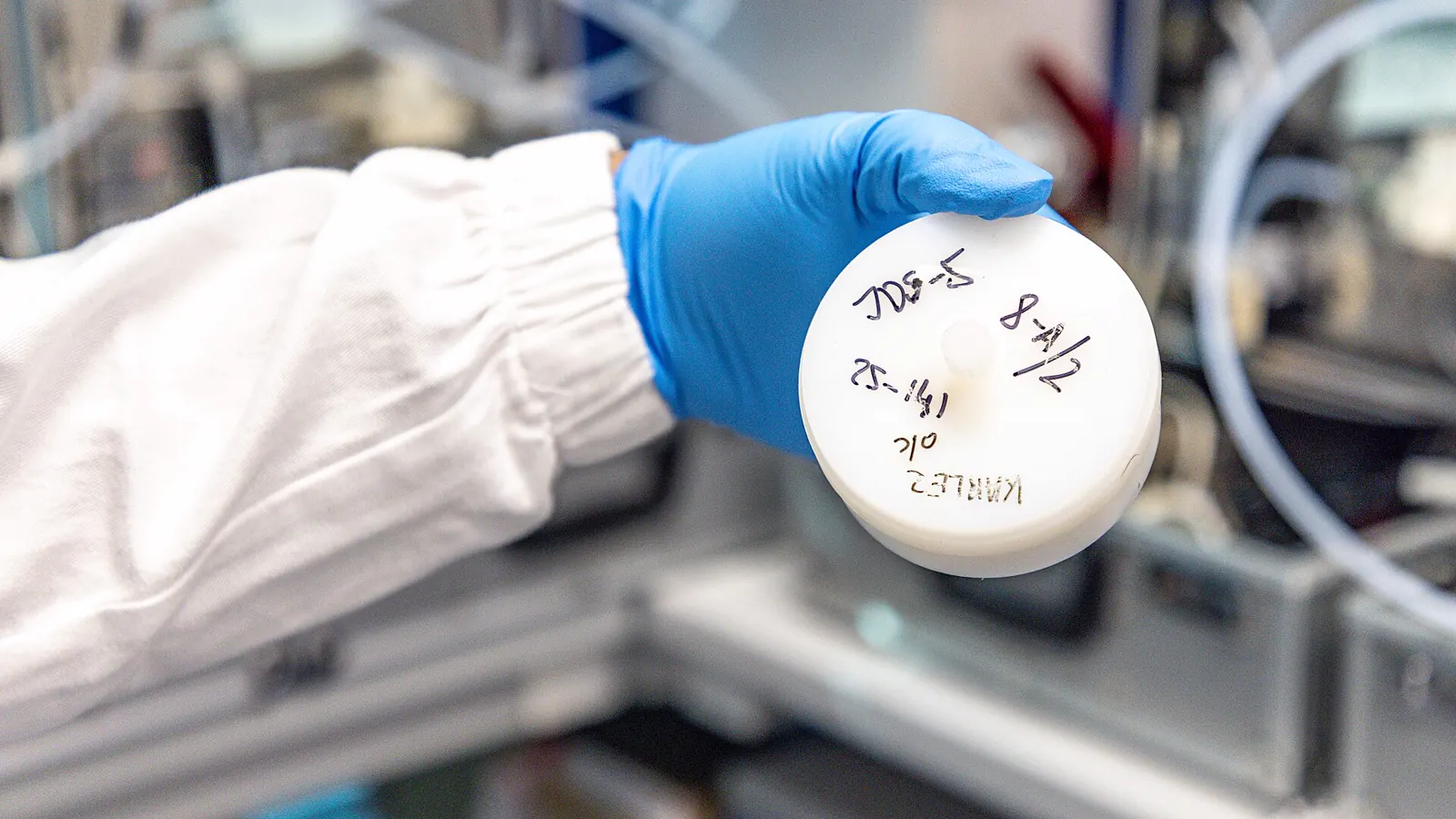 Gloved hand holding a labelled sample container, the batch identification a certificate of analysis refers to