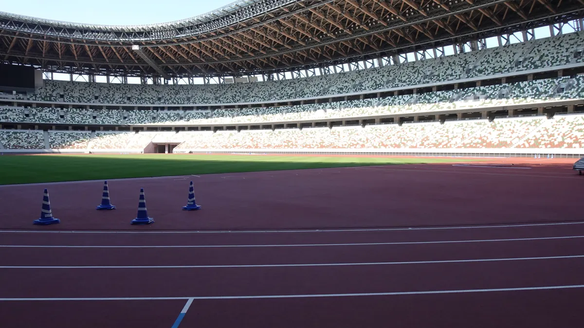 Empty athletics stadium with a red running track and tiered seating used for international competition
