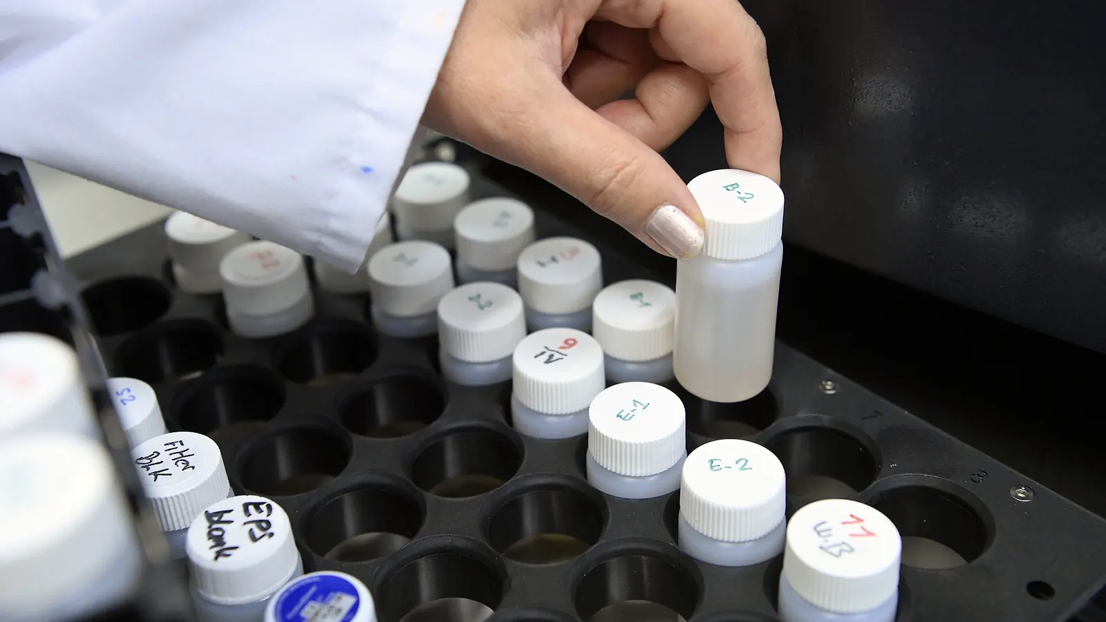 Hand placing capped sample containers into a laboratory rack, the kind of vial format research peptides are handled in
